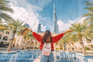 Woman in a red sweater stands with arms raised in front of Dubai Tower, celebrating the vibrant cityscape.rent a car in dubai